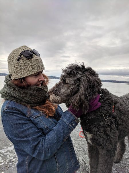 Celeste, a dog trainer, standing with a gray shaggy dog at the edge of an ocean, from FurHaven Pet Products